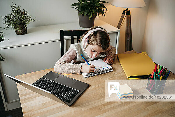 Mädchen macht Hausaufgaben und sitzt zu Hause mit Laptop am Tisch