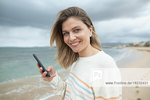Smiling beautiful blond woman using smart phone at beach