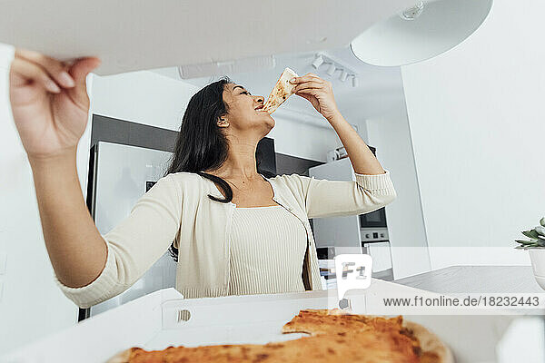 Happy young woman eating pizza at home