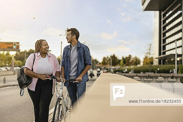 Happy woman and man walking with bicycle at footpath