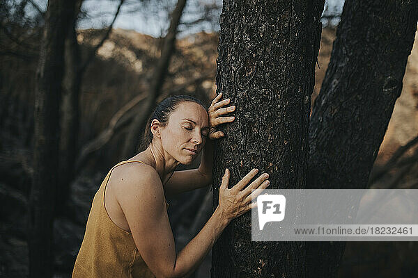 Woman with eyes closed leaning on burnt tree trunk