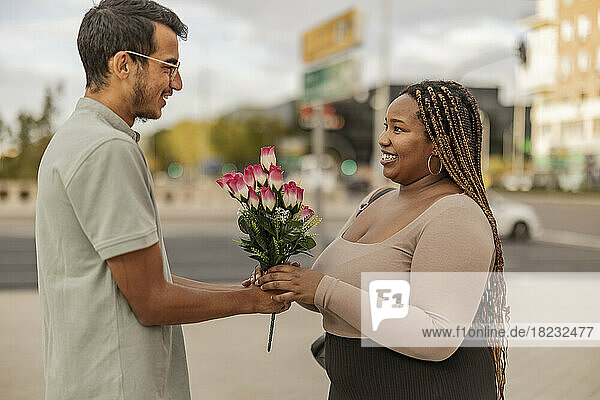 Junger Mann schenkt Freundin am Fußweg einen Blumenstrauß