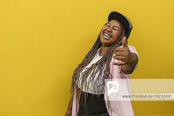 Fröhliche Frau lacht und gestikuliert vor gelber Wand