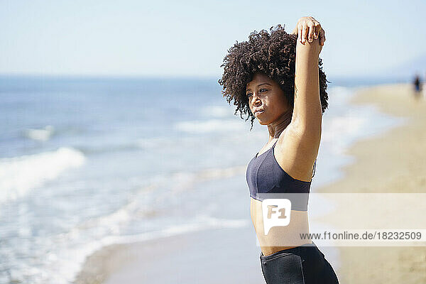 Young woman stretching at beach on sunny day