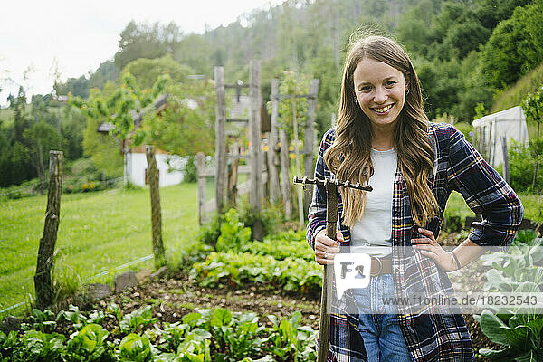 Happy woman standing with rake in vegetable garden
