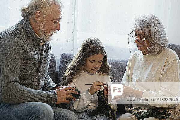 Großeltern bringen ihrer Enkelin auf der Couch das Häkeln bei