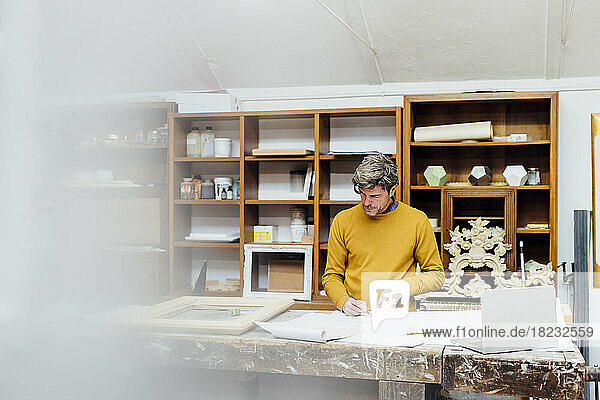 Mature craftsman sketching standing at workbench in workshop