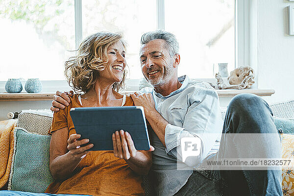 Glückliches älteres Paar  das zu Hause mit einem Tablet-Computer auf dem Sofa sitzt