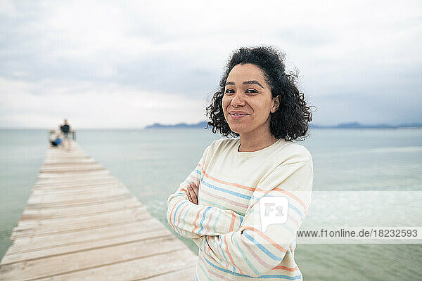 Happy woman with arms crossed standing on jetty