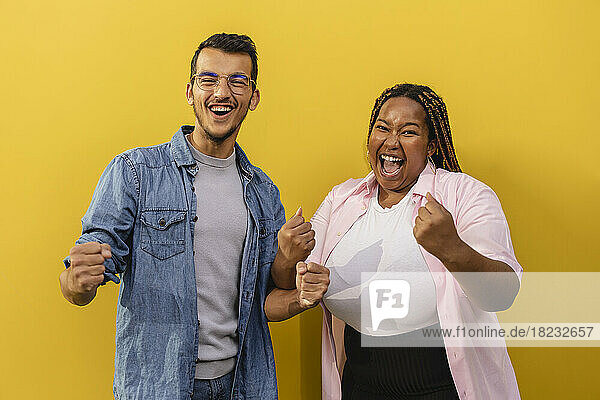 Cheerful young couple standing with closed fists in front of yellow wall