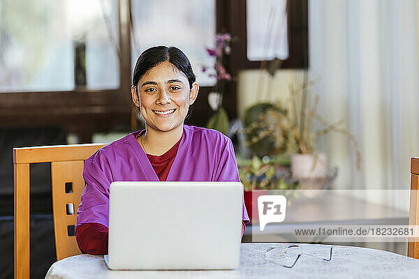Smiling young nurse sitting with laptop at home