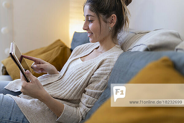 Happy young woman using tablet computer on sofa at home