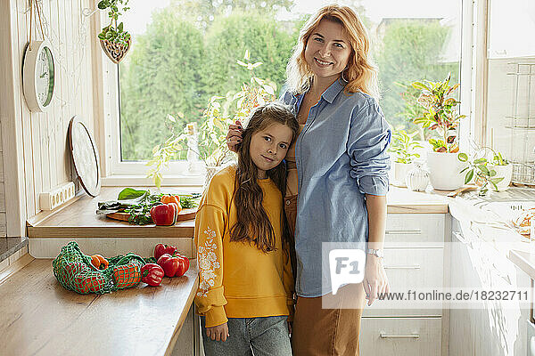 Portrait of smiling mother with her daughter in kitchen
