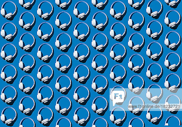 Pattern of rows of headphones flat laid against blue background