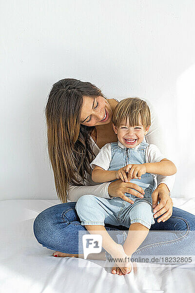 Smiling woman playing with son sitting on bed at home