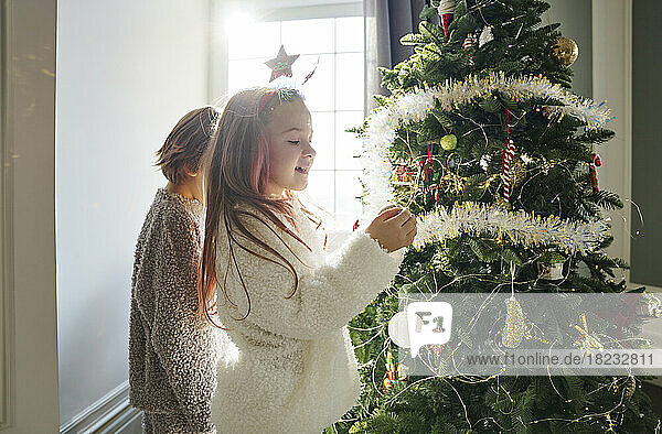 Glückliches Mädchen mit Bruder  der zu Hause im Schlafzimmer den Weihnachtsbaum schmückt