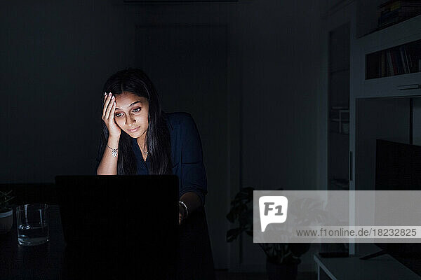 Besorgte Frau mit Kopf in der Hand  die auf Laptop schaut