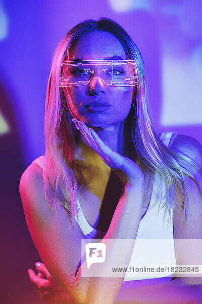 Young woman wearing smart glasses with neon lighting in front of wall