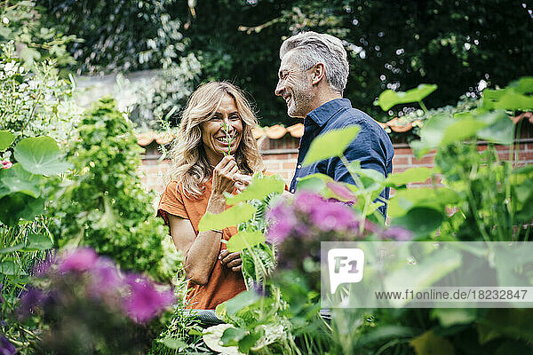 Happy man with woman holding leaf standing behind flowering plants