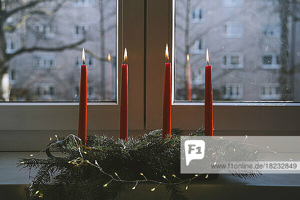 Burning red candles on advent wreath in front of window at home