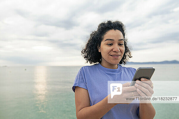 Smiling woman using mobile phone in front of sea