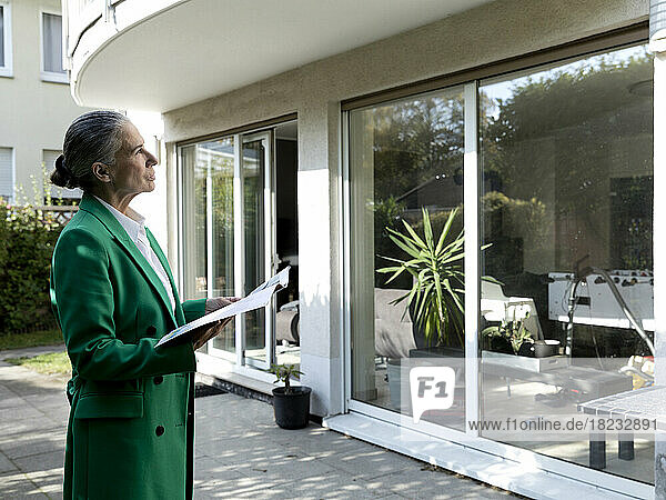 Senior businesswoman holding file looking at house