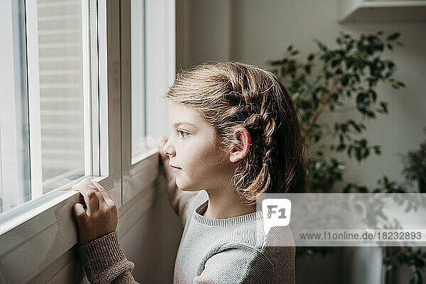 Thoughtful girl looking through window at home