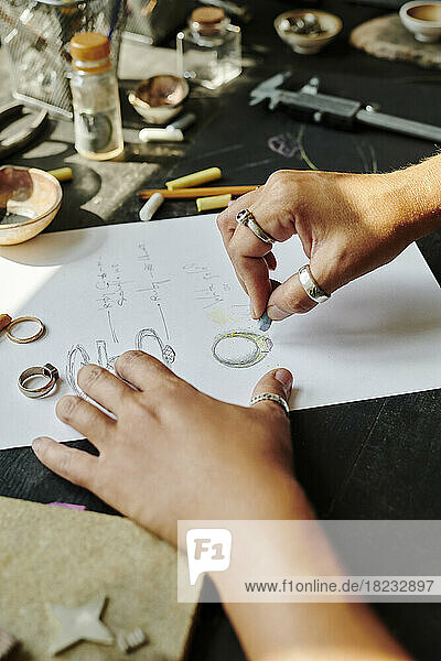 Hände eines Juweliers skizzieren Ringdesign auf Papier an der Werkbank