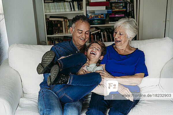 Glückliches Mädchen mit Vater und Großmutter  die es zu Hause auf dem Sofa genießen