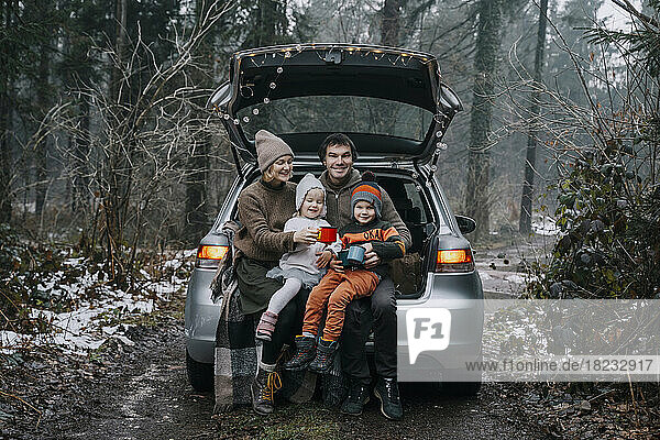 Glückliche Familie mit Kaffeetassen  die Zeit miteinander im Kofferraum eines Autos verbringt