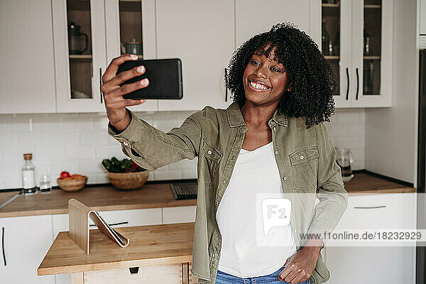 Lächelnde Frau  die zu Hause in der Küche ein Selfie mit dem Smartphone macht