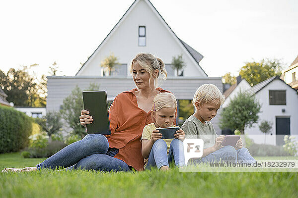 Familie mit drahtlosen Technologien sitzt auf Gras im Garten