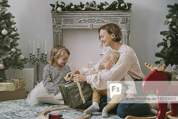 Mother wrapping Christmas gift with children at home