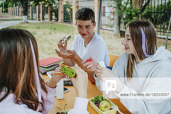 Girls with boy having lunch sitting at table in schoolyard