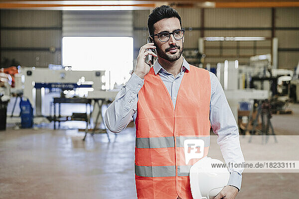 Engineer wearing protective workwear talking on smart phone in industry