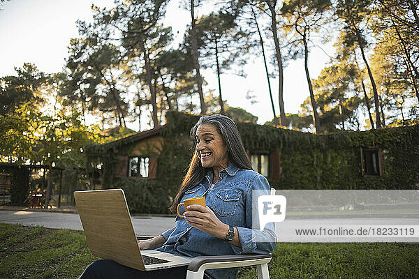 Lächelnde reife Frau  die draußen mit Laptop sitzt