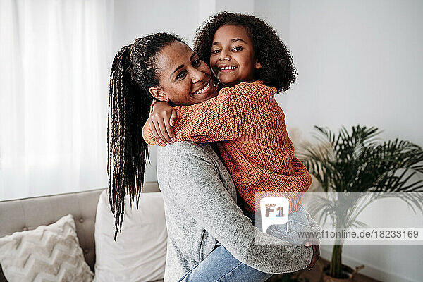 Happy woman carrying and embracing daughter in living room at home