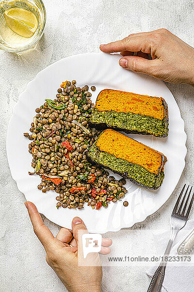 Personal perspective of woman touching plate of carrot and spinach terrine with lentil salad