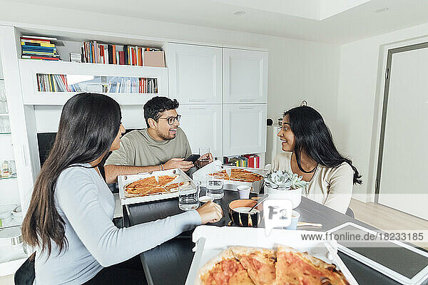 Happy women and man having pizza at dining table in living room