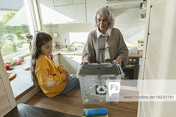 Grandmother and granddaughter sorting recycling waste in kitchen