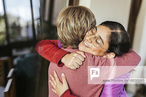 Happy young caregiver hugging senior woman at home