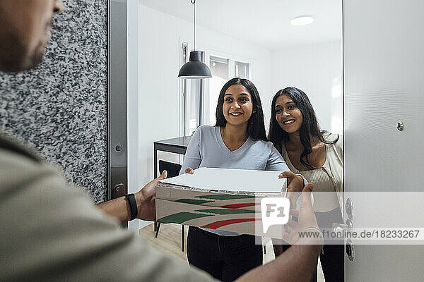 Smiling young women receiving pizza from delivery person