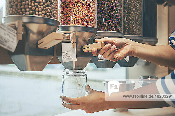 Hände einer Frau halten Einmachglas unter Lebensmittelspender im Geschäft