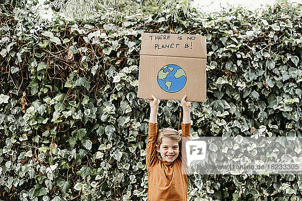 Glückliches Mädchen mit erhobenen Armen  das ein Banner mit Botschaft und Planetenzeichnung vor der Pflanze hält