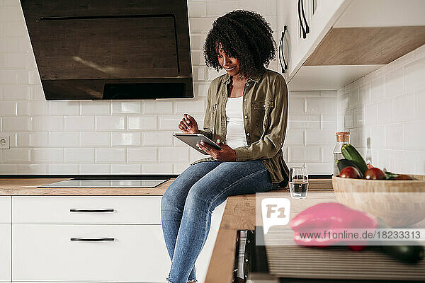 Frau sitzt zu Hause auf der Küchentheke und benutzt einen Tablet-PC