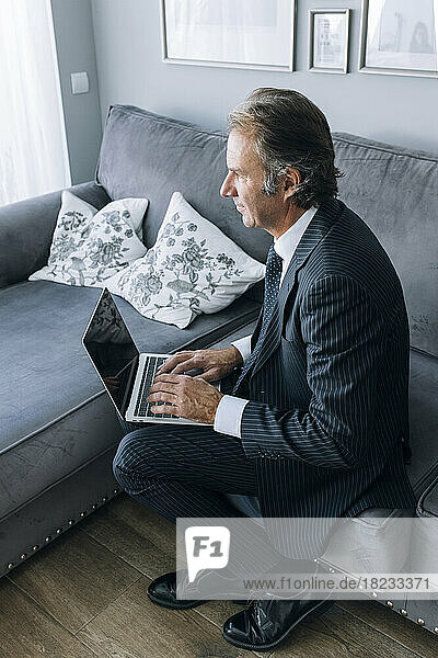 Nachdenklicher Geschäftsmann mit Laptop auf dem Sofa  der zu Hause arbeitet