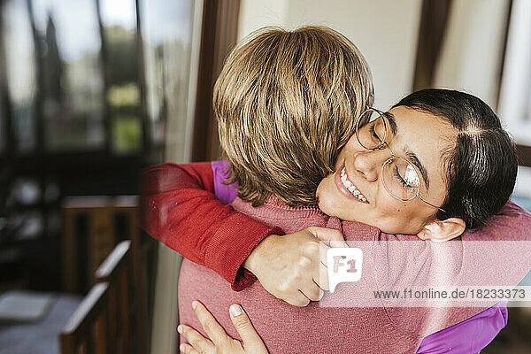 Happy caregiver hugging senior woman at home