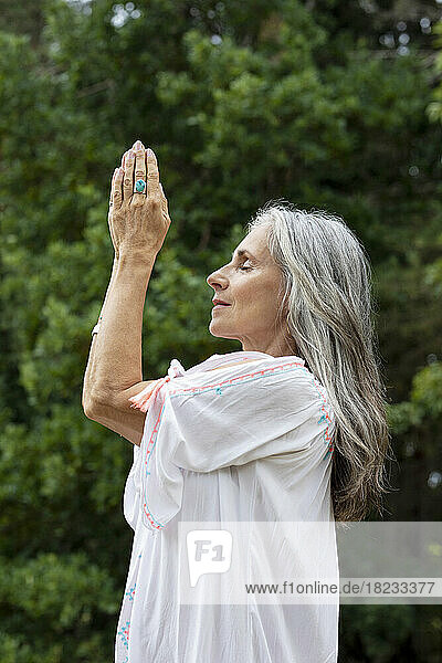 Mature woman meditating with hands clasped in forest