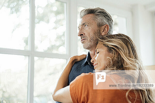 Smiling woman embracing man in front of window at home