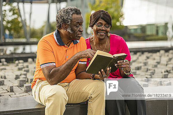 Senior couple reading book sitting on wall